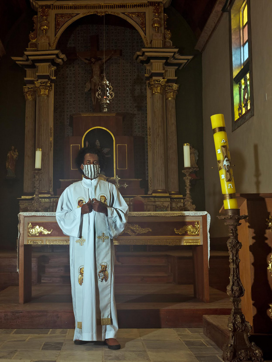 an African American priest wearing white robes and standing inside a church