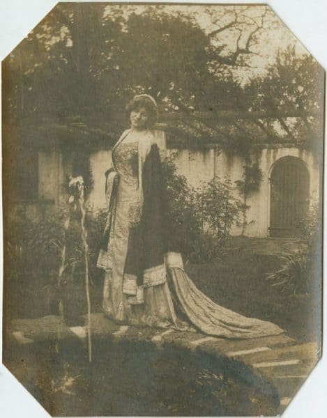 Shown in the garden, the subject stands in front of the pergola next to a fountain (bottom left).
