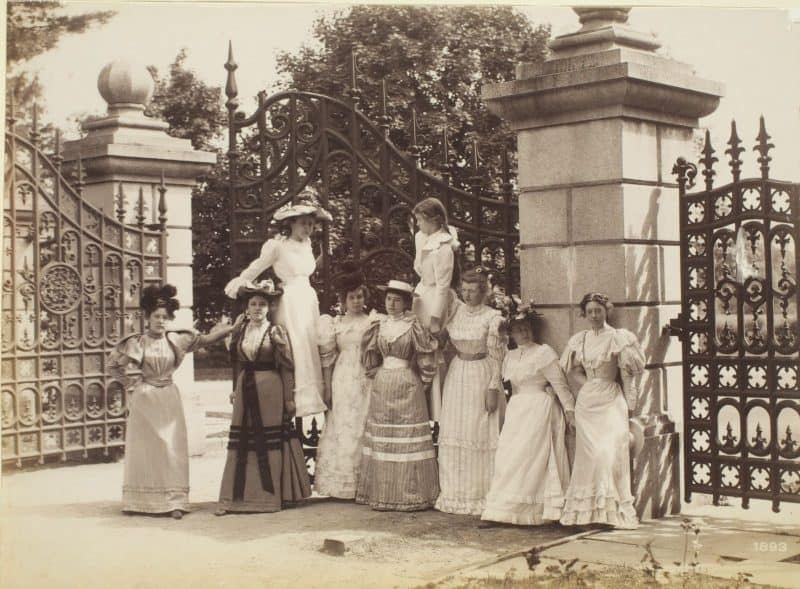 Group of well-dressed women posed before a large gate.