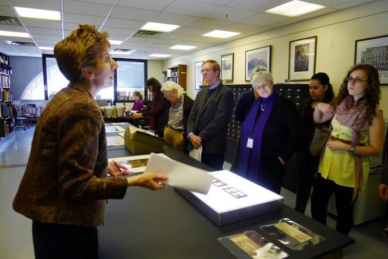 Sarach Weatherwax presents information to a group of visitors in the Print Department. The table between them is laid out with collections items.