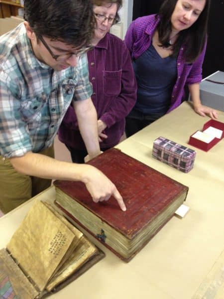 Three people inspect the bindings of a large, red book.