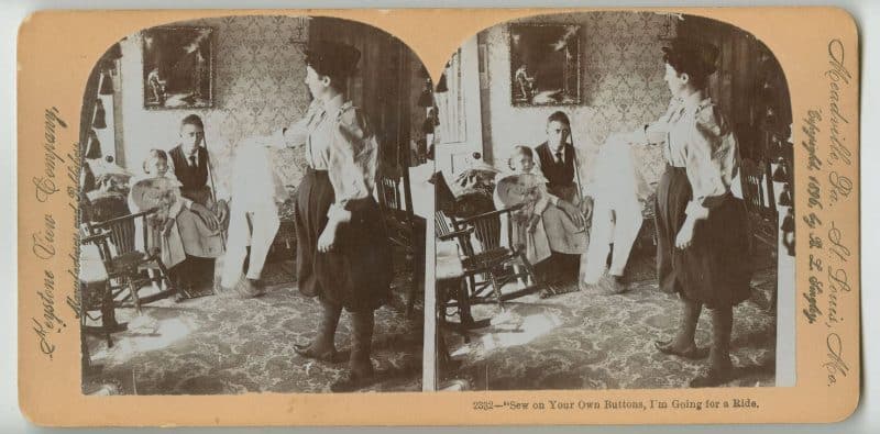 Stereograph depicting a woman in breeches holding out a pair of drawers towards a seated man and child. The man wears an apron and holds a broom.