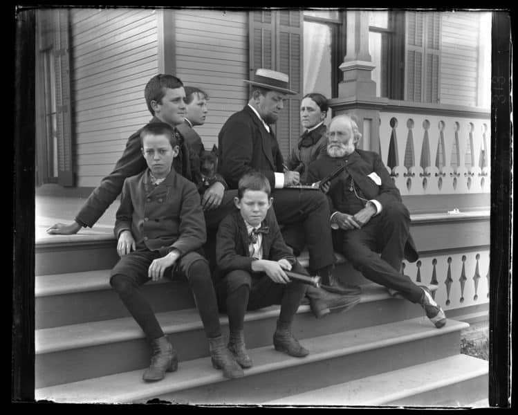 A group of seven sit on the porch staircase, posed.