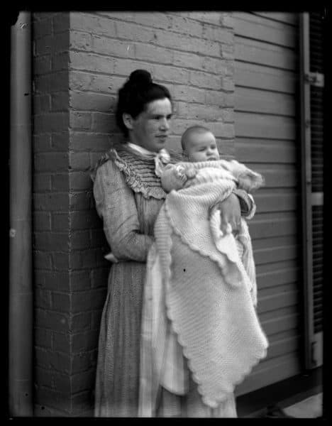Marriott C. Morris, J.R.M. [Jane Rhoads Morris] & baby, ca. 1900. Morris stands against a brick wall and holds a baby in a blanket.