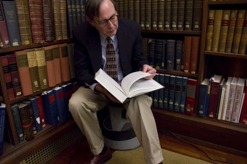 Librarian Jim Green sitting on a library stool and paging a book.