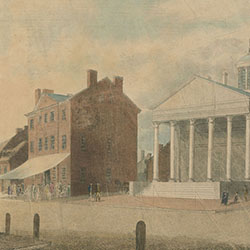 Urban street scene including six-columned classical style building and several others. Mostly male pedestrians are on sidewalk, including man pushing wheelbarrow
