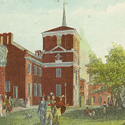 Pedestrians including Indigenous people walk around grassy area next to large brick building. Building includes steeple and clock tower
