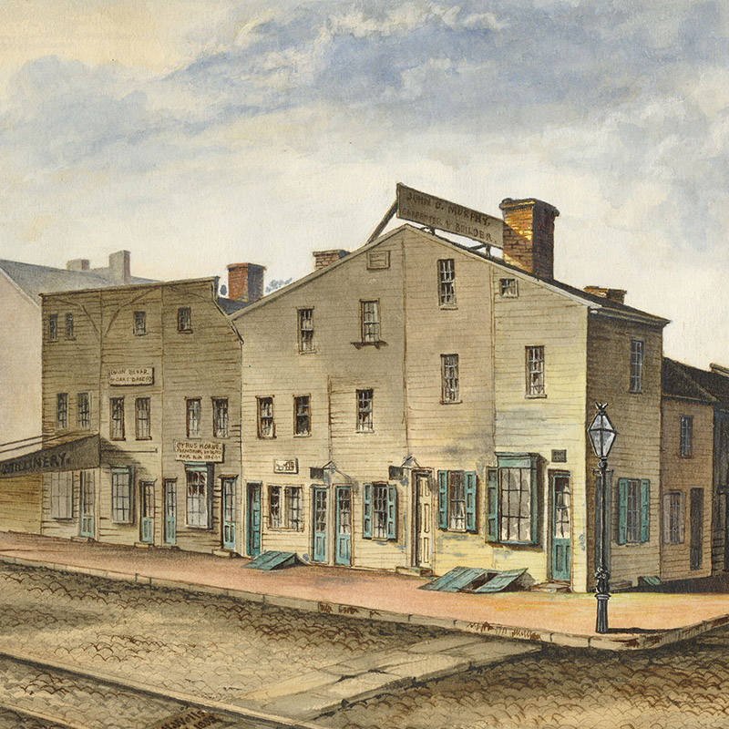 Watercolor depicting street corner lined with wooden buildings. Some of the buildings are adorned with signs.