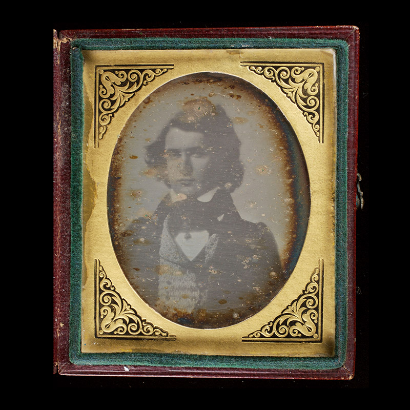 Half-length portrait of young white man, facing slightly left, and attired in jacket, vest, and wide neck tie. In gold mat in red leather case.