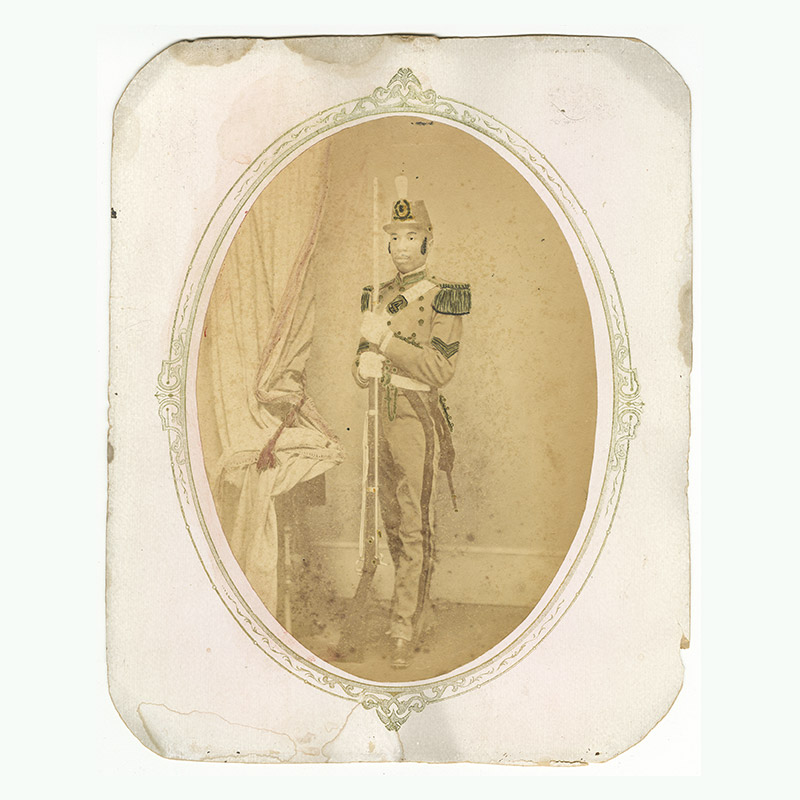 Full-length portrait of Black man in militia uniform. Man holds a rifle. Photo contains touch up marks.