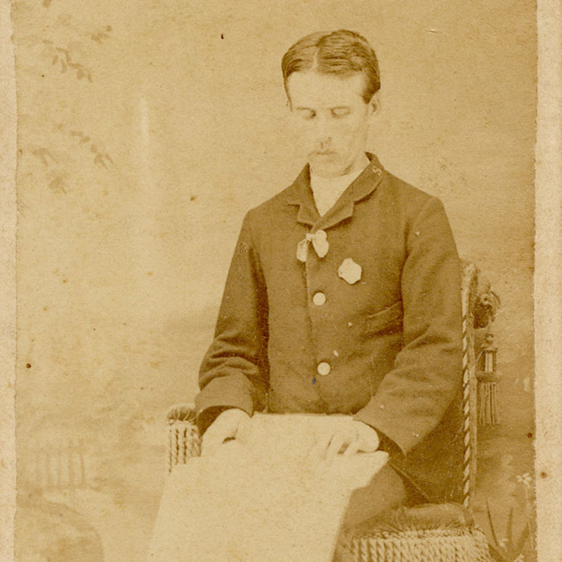 Full-length portrait of young, blind, seated white man reading a book with his fingers.