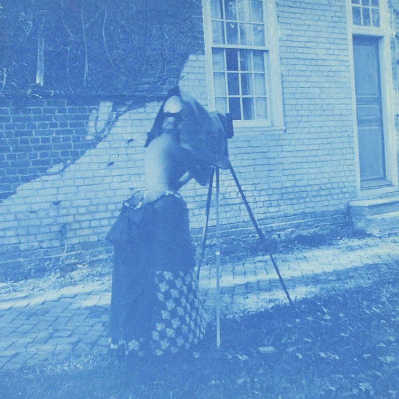 Blue color photographs showing a woman under hood of standing camera and room with 18th-century furniture and paintings. 