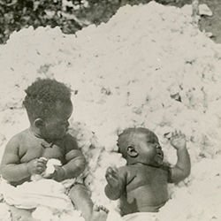 Black and white photograph of a toddler and a baby in a pile of cotton