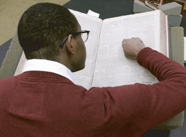 For Scholars button: Black researcher in glasses studies a book with his finger on the text.