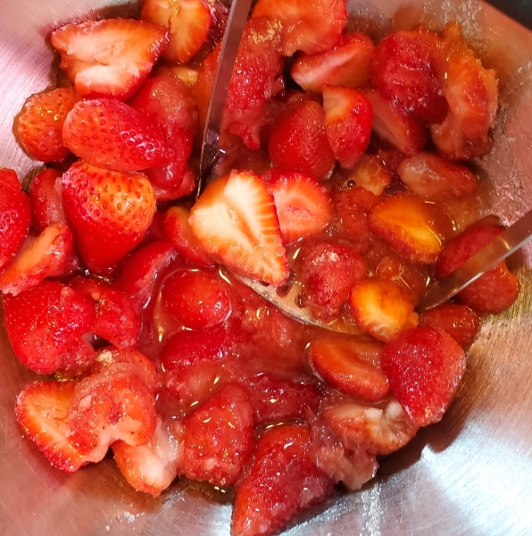 Strawberries and sugar mixed in bowl.