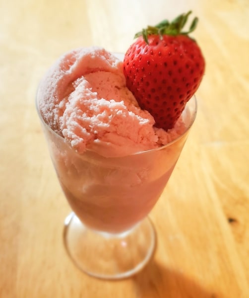 Strawberry ice cream in a glass serving dish with a fresh strawberry.