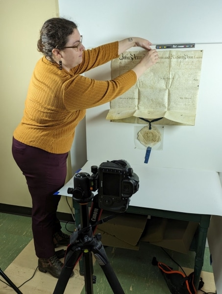Photograph of a white woman with brown hair using magnets to prepare an oversized item to hang on a wall for imaging