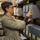 Photograph of a white woman with short brown hair and glasses putting a box of archival items back on a shelf