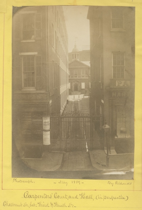 Photograph of Carpenters' Hall visible down a long alleyway, mounted on yellow paper with handwritten notations of place, date, and photographer