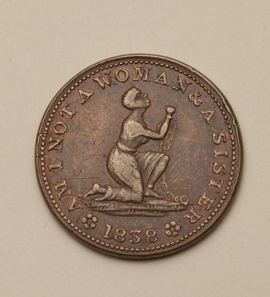 Photograph of medal with woman kneeling with raised arms in chains and text that reads Am I Not a Woman and a Sister 1838