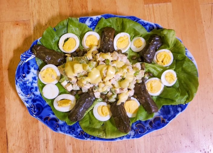 Chicken salad served on a platter with hard boiled eggs and stuffed grape leaves