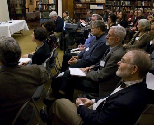 Photograph depicting a crowd of attendees sitting and watching a presentation.