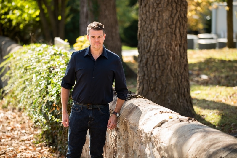 Photo of Jim Downs standing outside beside a wall and a tree